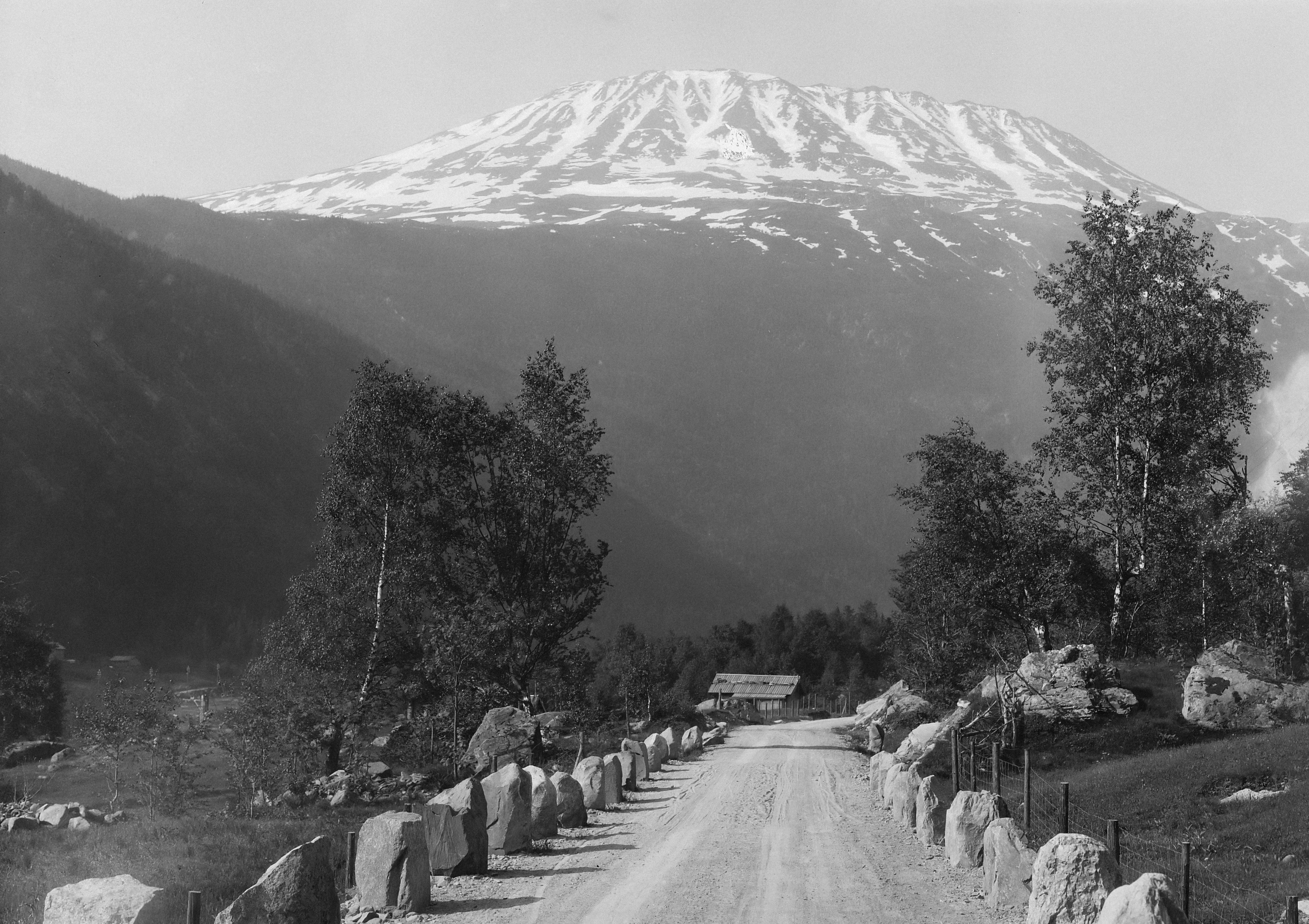 ein Schwarz-Weiß-Foto einer Straße mit einem Berg im Hintergrund