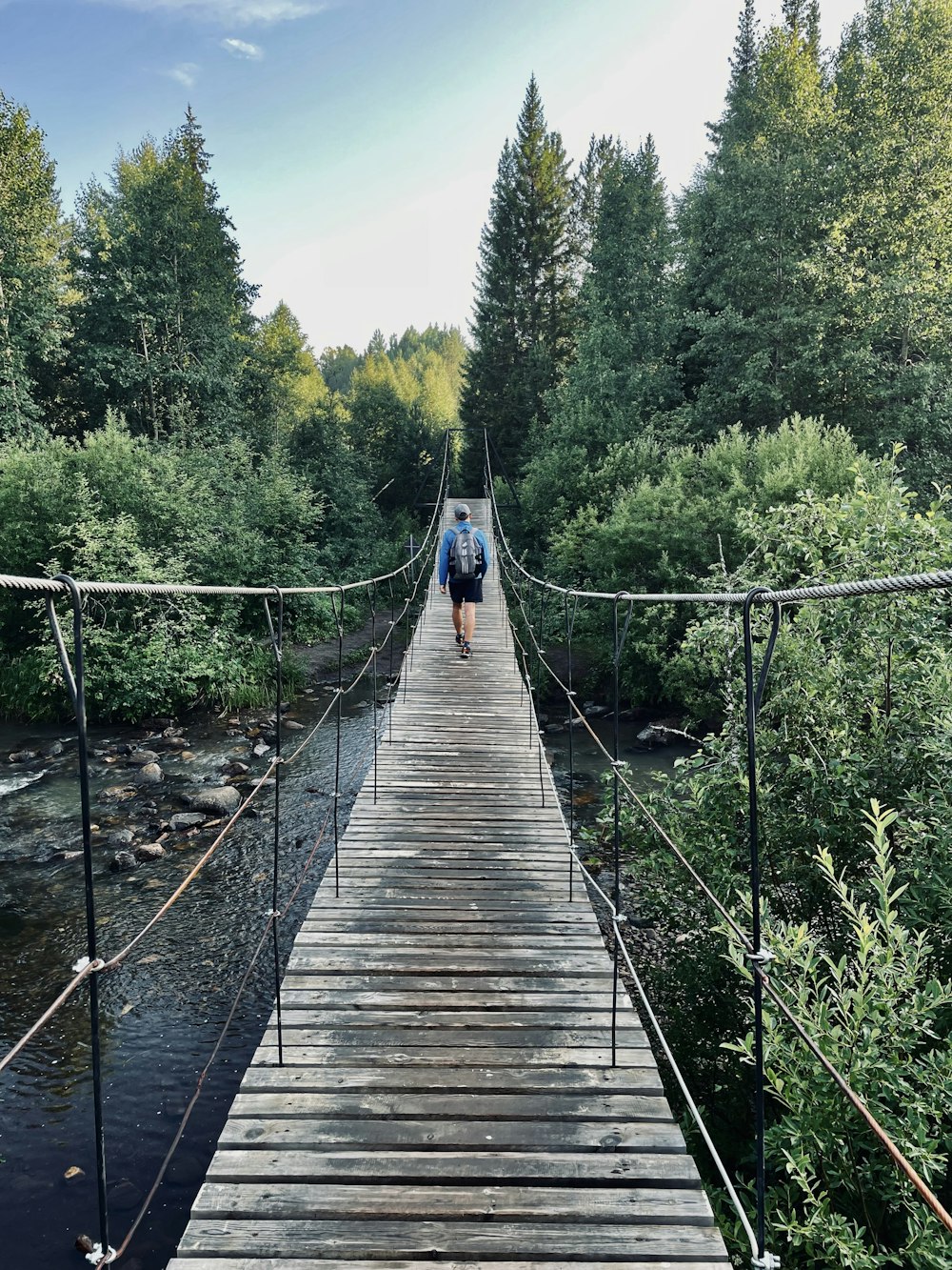 a man walking across a suspension bridge over a river