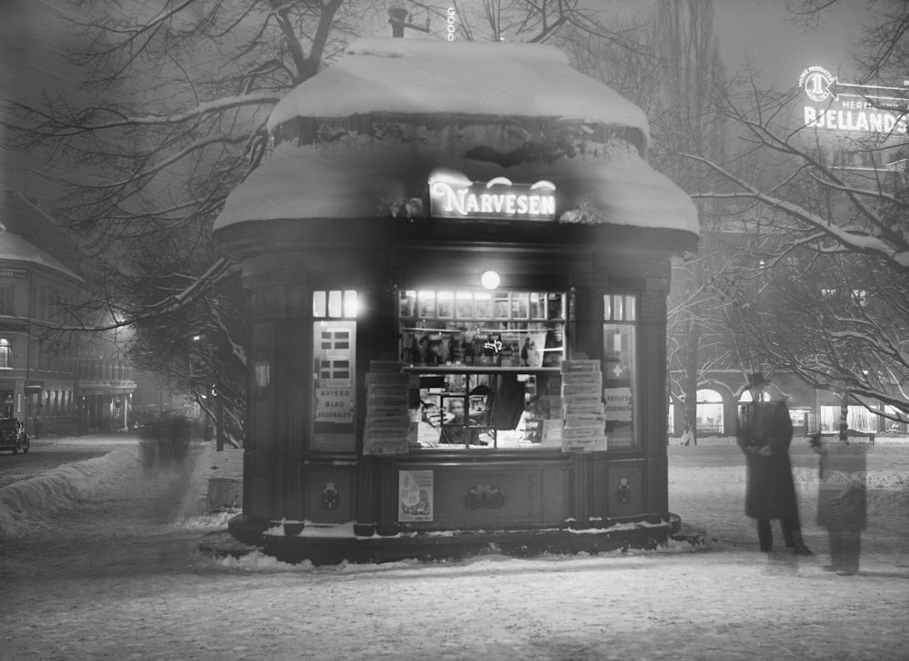 a black and white photo of a man standing in front of a kiosk