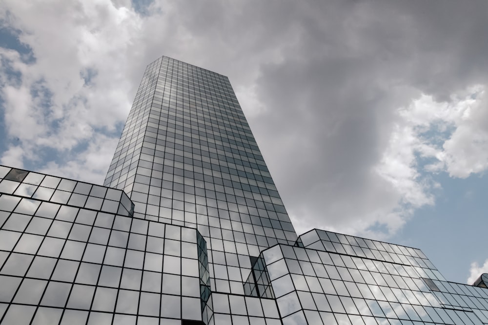 a tall glass building with a cloudy sky in the background