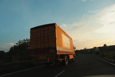 A sleek modern truck with orange accents driving on a highway at dusk under a moody sky.