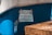A handwritten sign is taped to the side of a blue vehicle or object. The sign is made of paper with text in Polish, secured with pieces of tape at the corners. There is a wicker basket or similar object partially visible in the foreground.