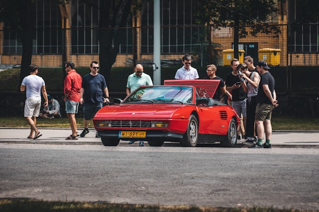 A diverse group of car enthusiasts gathered around a vintage car, sharing stories and laughter.