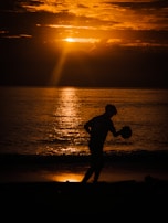 Sunset silhouette of a player throwing a baseball, embodying dedication and focus.