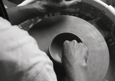 Hands shaping soft clay on a potter's wheel, bathed in natural light, capturing the art of making.