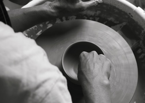 Hands mold a clay pot on a spinning pottery wheel, capturing the tactile artistry of pottery-making in motion.