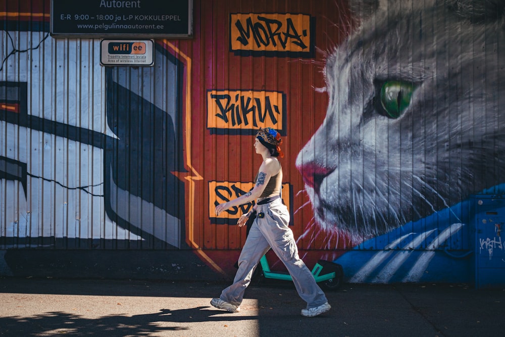 a woman walking down a sidewalk past a wall with a painting of a cat on