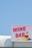 A bright and colorful sign displaying the words 'Wine Bar' with artistic illustrations of a wine glass and grapes. The sign is mounted on a structure against a clear blue sky backdrop.