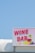 A bright and colorful sign displaying the words 'Wine Bar' with artistic illustrations of a wine glass and grapes. The sign is mounted on a structure against a clear blue sky backdrop.