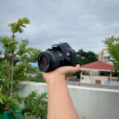 A vibrant photo of a photographer holding a sleek digital camera outdoors.