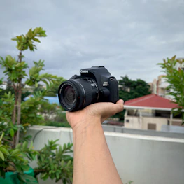 A vibrant photo of a photographer holding a sleek digital camera outdoors.