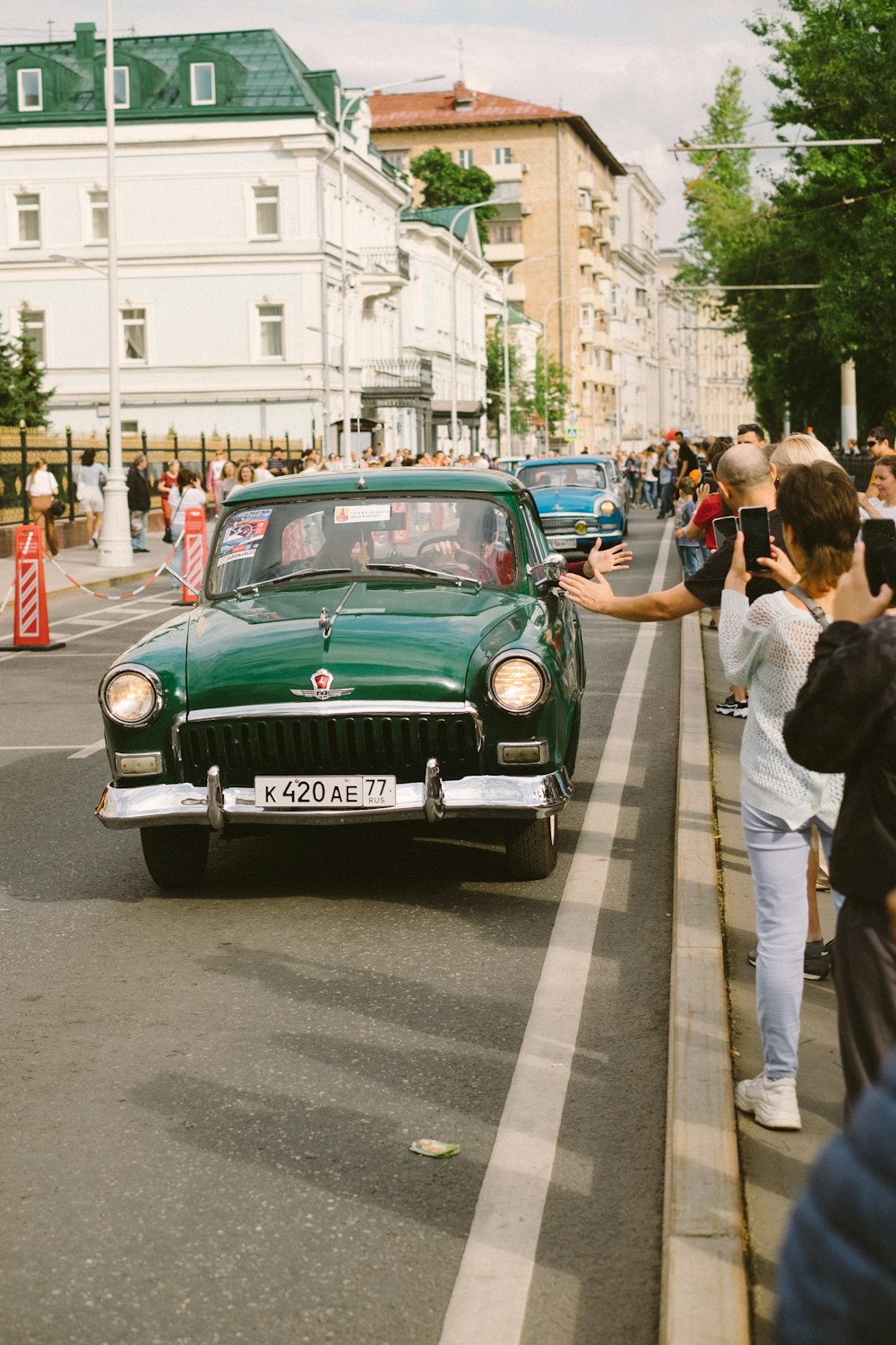 a green car driving down a street next to a crowd of people
