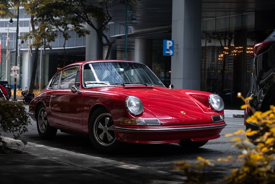A sleek red compact car parked on a city street under soft sunlight.