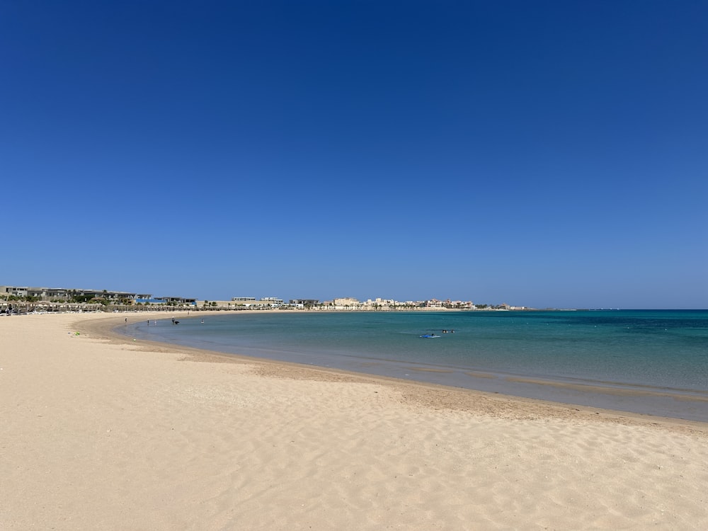 a sandy beach with clear blue water and buildings in the background