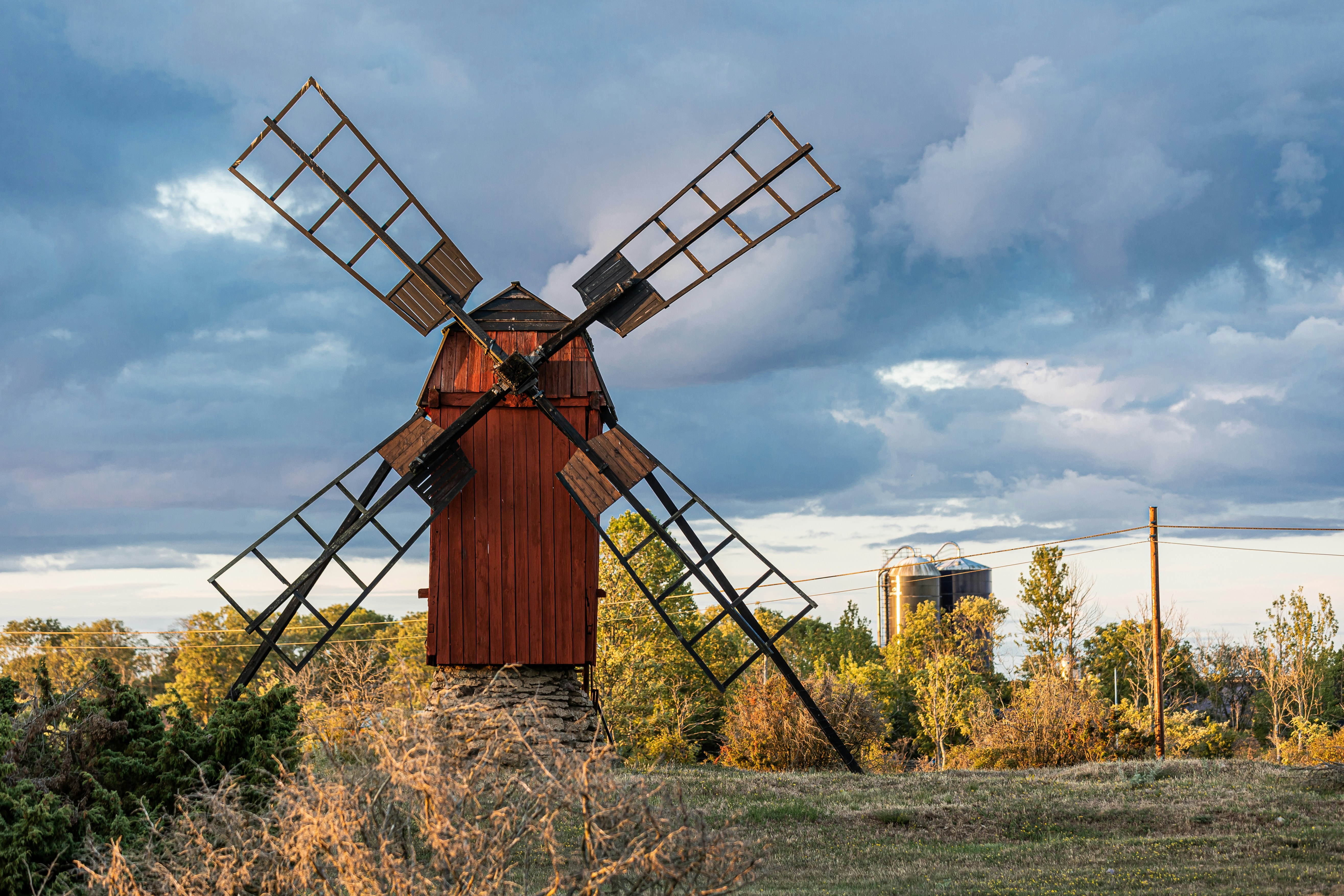 a windmill in a field with trees and clouds in the background