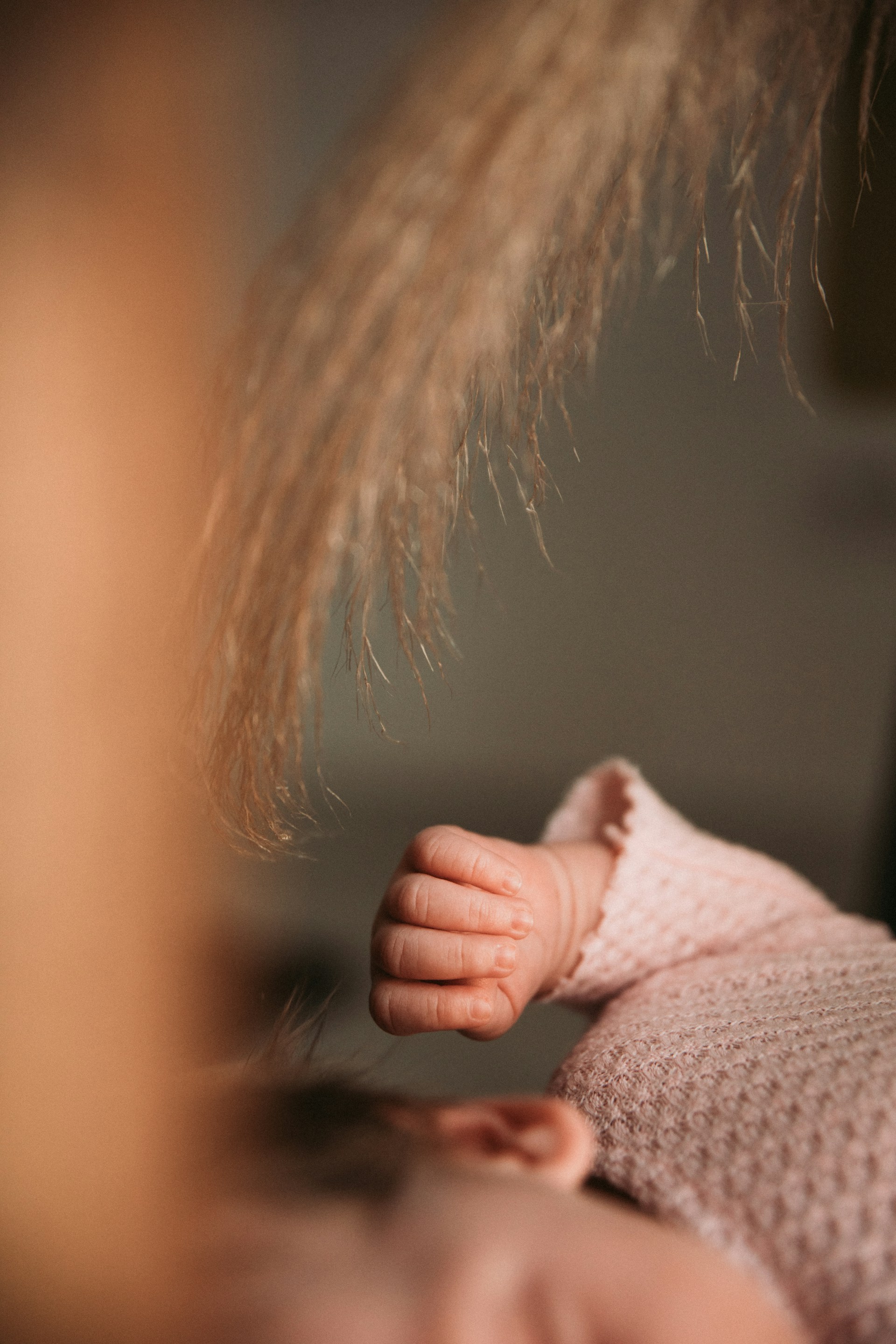 A close-up of delicate newborn hands resting on a plush, champagne gold blanket, highlighting the intimate and unscripted storytelling style.