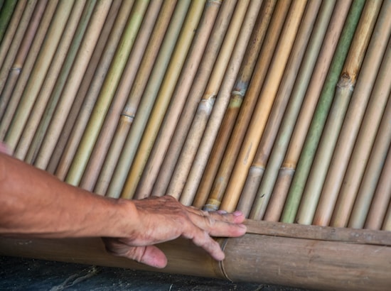 A hand rests gently on a surface made of closely arranged bamboo sticks. The bamboo sticks vary in color from light green to golden brown, showcasing natural textures and variations.