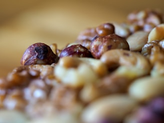 A close-up of mixed nuts including hazelnuts and walnuts, with a detailed texture and warm lighting. The focus is on the nuts, creating a sense of rich, natural texture.