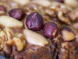 A close-up view of a baked item featuring whole hazelnuts, almonds, and walnuts embedded in a brown, textured surface.