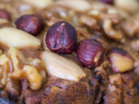 A close-up view of a baked item featuring whole hazelnuts, almonds, and walnuts embedded in a brown, textured surface.