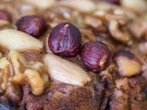 A close-up view of a baked item featuring whole hazelnuts, almonds, and walnuts embedded in a brown, textured surface.