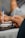 A close-up view of two hands holding pens, poised over a laptop keyboard. The focus is on the hands and the pens, with blurred figures in the background possibly working on the same task.