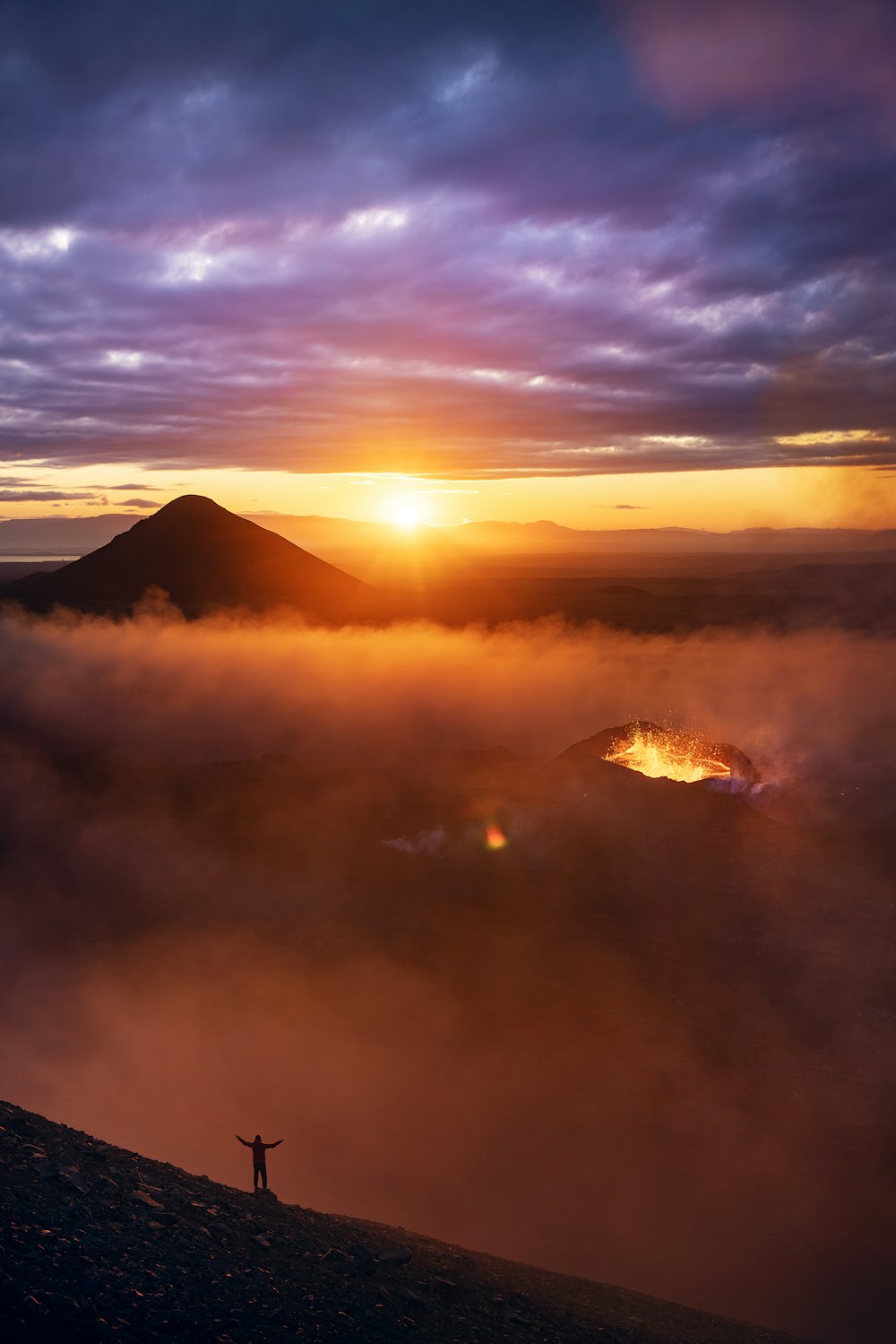 Una persona in piedi sulla cima di una collina con un tramonto sullo sfondo