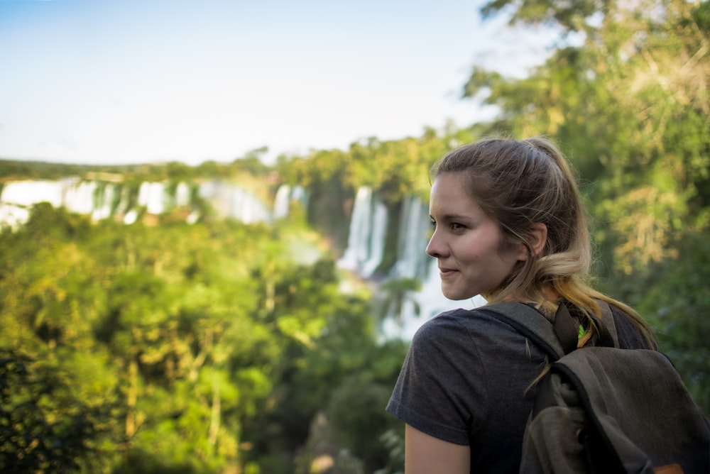 eine frau mit einem rucksack, die auf einen wasserfall schaut