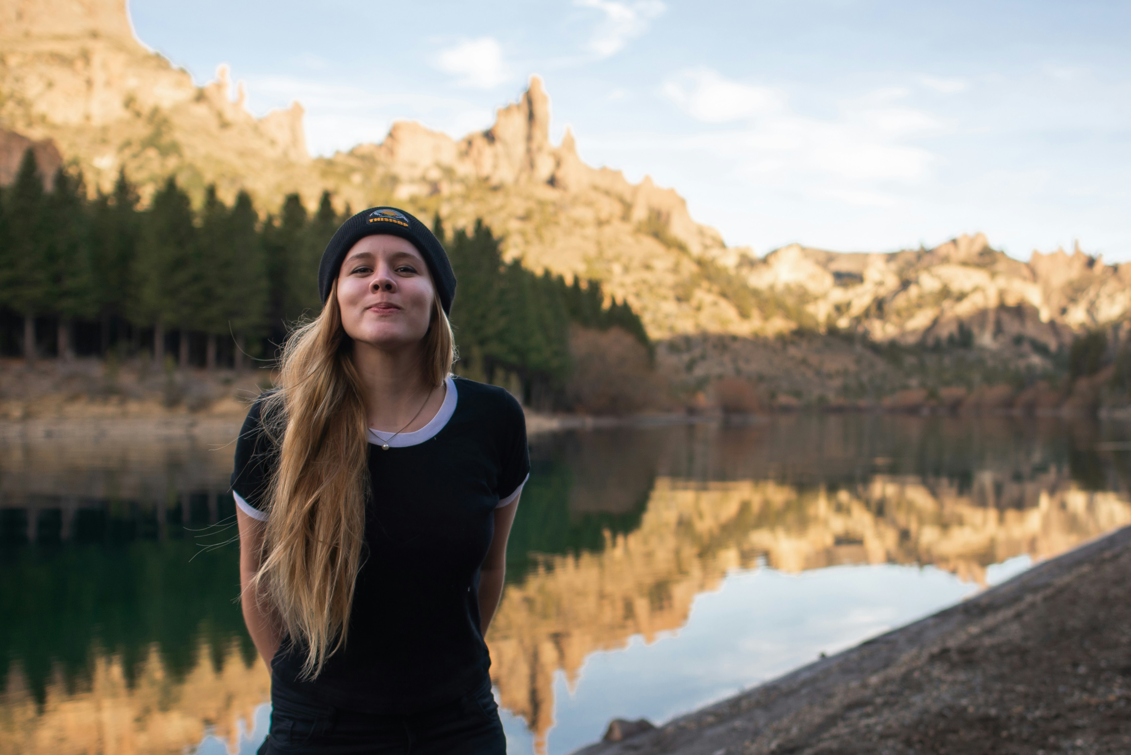 a woman standing in front of a lake with mountains in the background