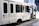 A white touring bus with the text 'Nashville Experience Tours' displayed on its side. The bus is decorated with balloons in white, blue, and gold. Social media handles are printed on the bus's exterior, including logos for Facebook and Instagram. The bus has multiple dark-tinted windows and is parked on a city street.