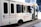 A white touring bus with the text 'Nashville Experience Tours' displayed on its side. The bus is decorated with balloons in white, blue, and gold. Social media handles are printed on the bus's exterior, including logos for Facebook and Instagram. The bus has multiple dark-tinted windows and is parked on a city street.