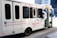 A white touring bus with the text 'Nashville Experience Tours' displayed on its side. The bus is decorated with balloons in white, blue, and gold. Social media handles are printed on the bus's exterior, including logos for Facebook and Instagram. The bus has multiple dark-tinted windows and is parked on a city street.