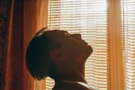 A serene lifestyle portrait of a person enjoying a quiet moment by a window with soft shadows.