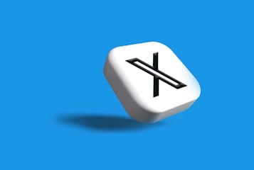 A white 3D cube with a black letter 'X' prominently displayed on one face, set against a vibrant blue background. The cube casts a subtle shadow, giving a sense of depth and dimension.