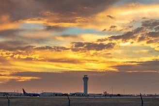 A bustling airport control tower overseeing planes taking off at sunset.