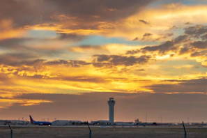 An air traffic control tower silhouetted against a vibrant sunset with planes taxiing below