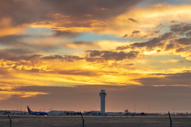 A vibrant control tower overseeing a busy airport runway at sunset.