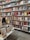 Bookshelves filled with a variety of books are organized neatly in a bookstore. The shelves hold an assortment of genres, including politics, science, and culture. A display table in the foreground showcases a small selection of highlighted titles.