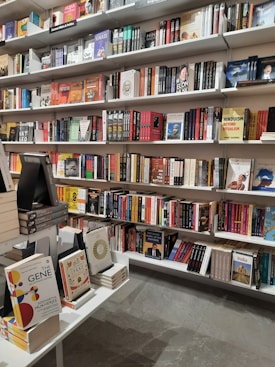 Bookshelves filled with a variety of books are organized neatly in a bookstore. The shelves hold an assortment of genres, including politics, science, and culture. A display table in the foreground showcases a small selection of highlighted titles.