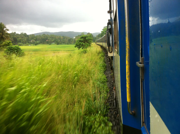 A scenic train winding through lush green hills under a bright blue sky.