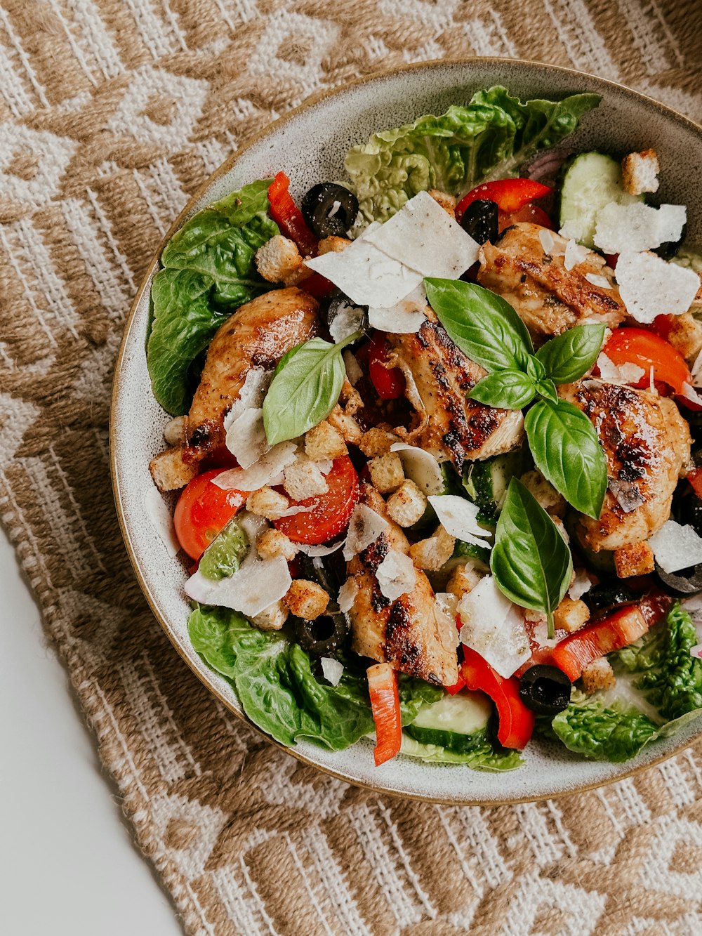 uma salada com frango, tomate, alface, azeitonas e queijo