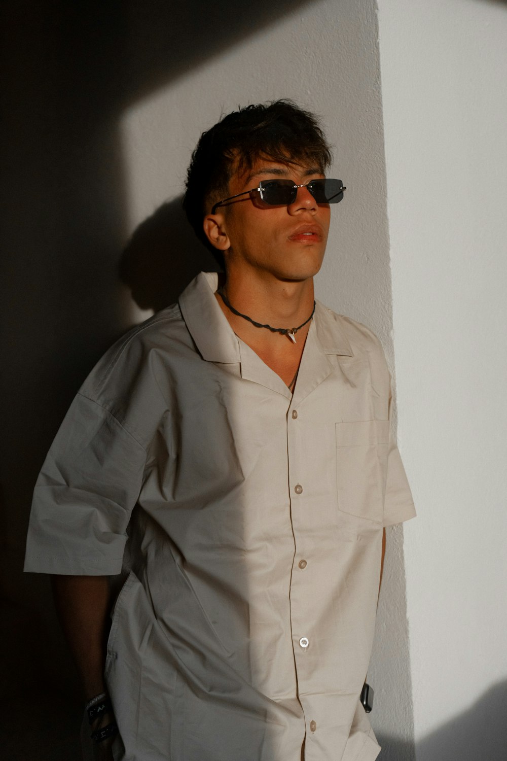 a man in a shirt and sunglasses leaning against a wall