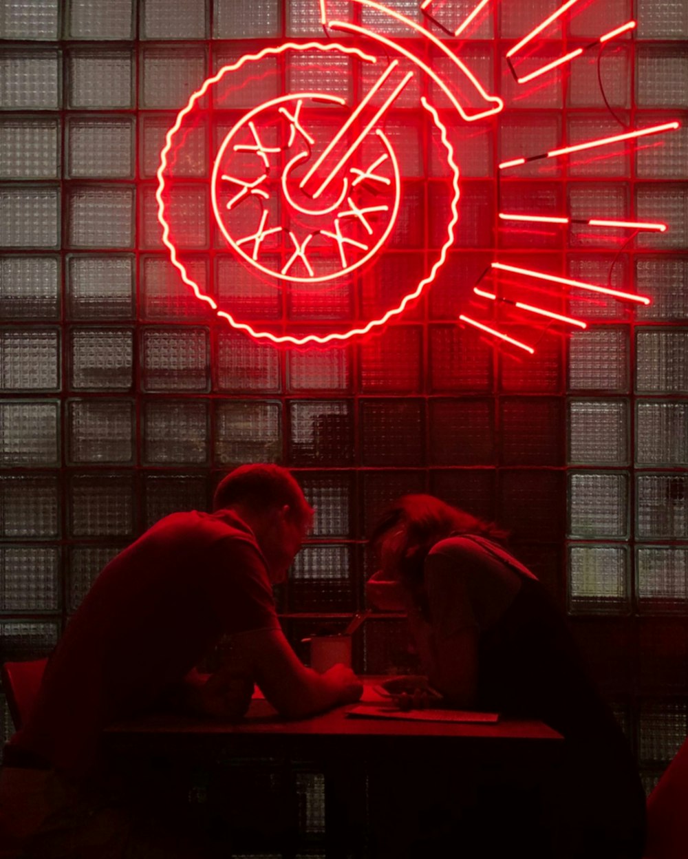 two people sitting at a table in front of a neon sign