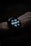 A close-up view of a smartwatch displaying the time, date, battery percentage, heart rate, and step count on its digital screen. The watch is worn on a wrist, and the background is dark, emphasizing the illuminated display.