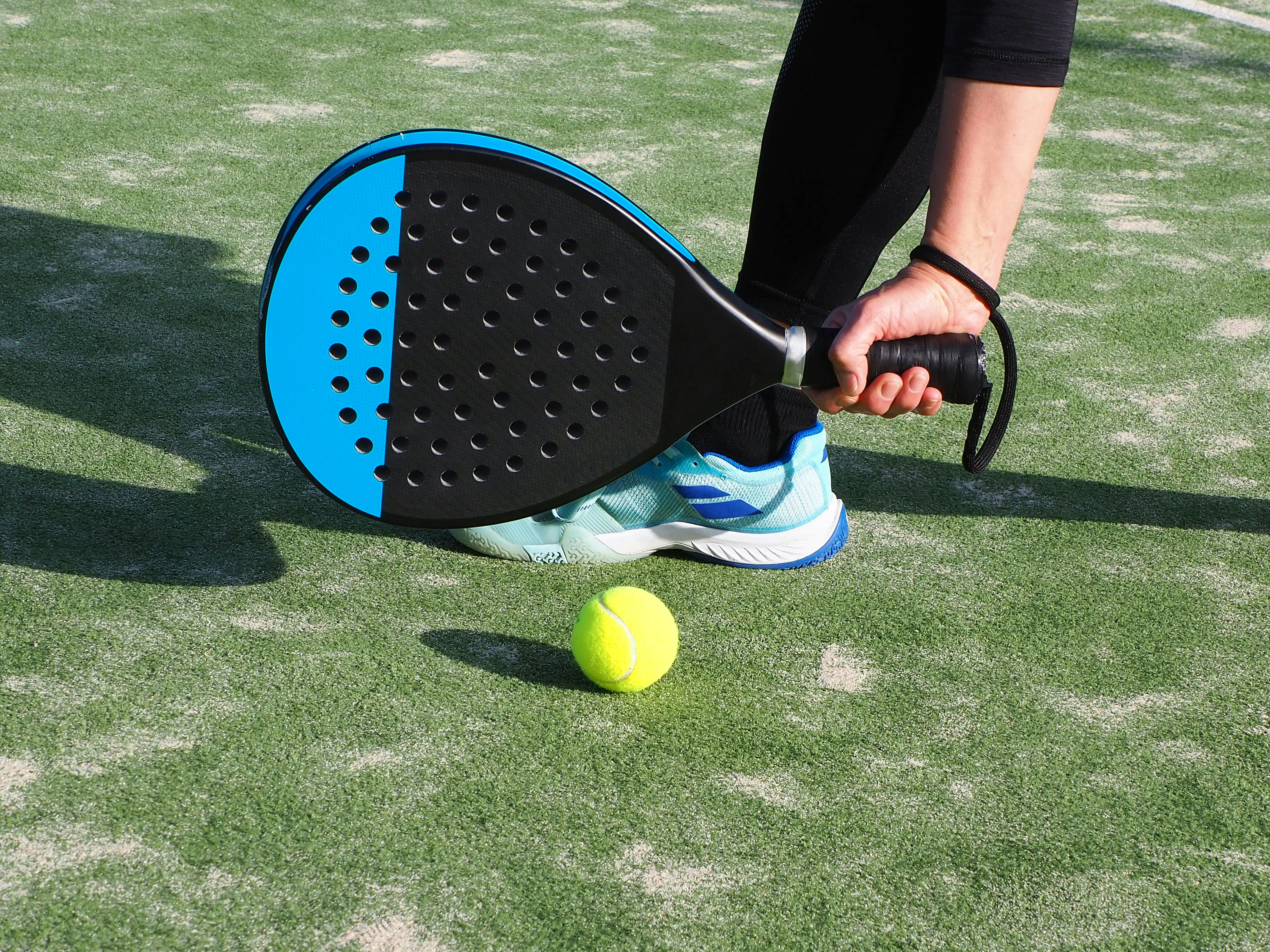 Yellow and black padel racket on green court surface