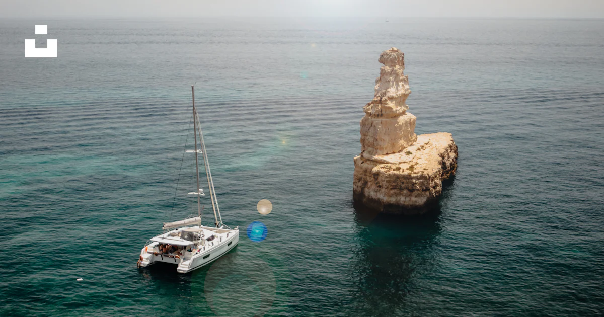 A sailboat floating in the ocean next to a rock formation photo – Free ...