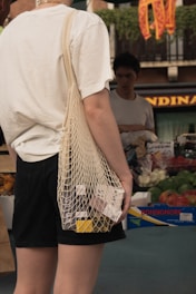 A person using reusable shopping bags at a local market filled with fresh produce.
