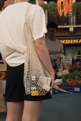 Smiling customer holding a small bag with fresh items, standing in front of a vibrant street market.