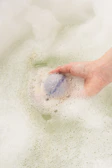 Hand holding a bath bomb releasing gentle bubbles in a serene spa setting.