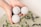 A pair of hands is holding three light-colored spherical objects, likely bath bombs, over a bath filled with water and floating lavender sprigs.